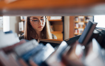 View through the shelves. Female student is in library that full of books. Conception of education.