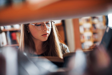 View through the shelves. Female student is in library that full of books. Conception of education.