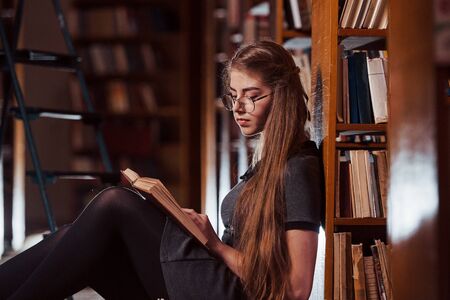 Sits on the floor. Female student is in library that full of books. Conception of education.の写真素材