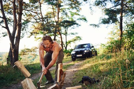 Woodsman with an axe cutting wood. Handsome shirtless man with muscular body type is in the forest at daytime.の写真素材