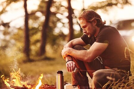 Enjoying the break. Man in black shirt near the campfire in the forest at his weekend time.の写真素材