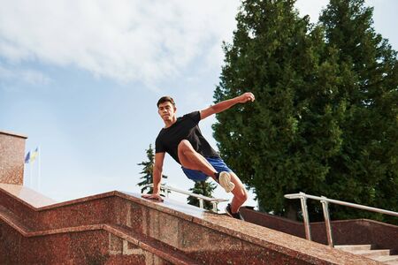 Above the obstacle. Young sports man doing parkour in the city at sunny daytime.の写真素材