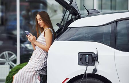 Woman on the electric cars charge station at daytime. Brand new vehicle.の写真素材