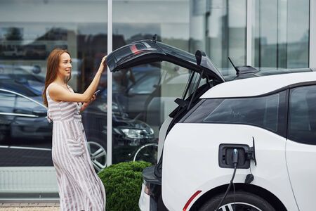Woman on the electric cars charge station at daytime. Brand new vehicle.の写真素材