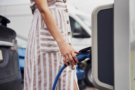 Woman on the electric cars charge station at daytime. Brand new vehicle.