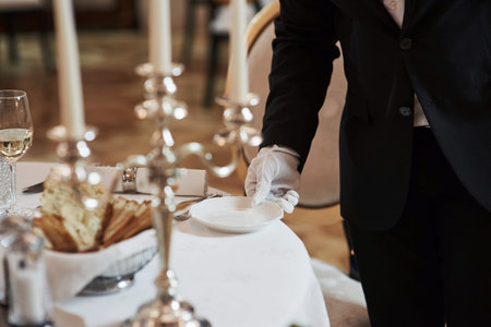 Holds white plate. Process of preparing place for special visitors. Waiter in classical wear works...