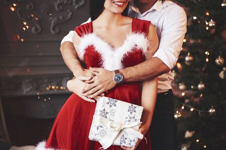 Manly hands hugs that smiled woman. Beautiful couple celebrating New year in the decorated room with Christmas tree behind.の写真素材
