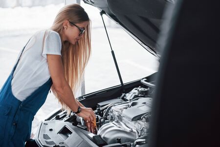 Cameramen hiding behind other vehile. On the lovely job. Car addicted woman repairs black automobile indoors.の写真素材