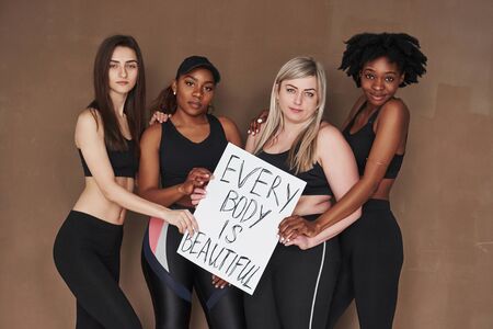 Every body is beautiful, sign. Group of multi ethnic women standing in the studio against brown background.の写真素材