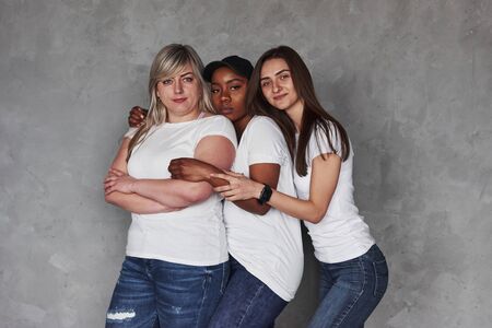 In same clothes. Group of multi ethnic women standing in the studio against grey background.の写真素材