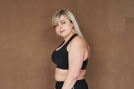 Looks into the camera. Blonde woman in the studio standing against brown background.の写真素材