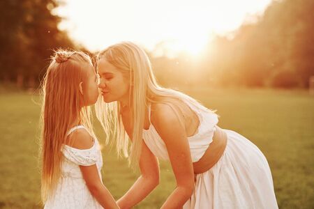 Kissing the child. Mother and daughter enjoying weekend together by walking outdoors in the field. Beautiful nature.の写真素材