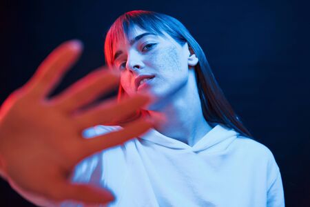 In white wear. Studio shot in dark studio with neon light. Portrait of young girl.の写真素材