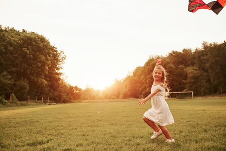 Kite is in the skye. Happy girl in white clothes have funin the field. Beautiful nature.の写真素材