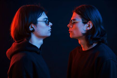 Looking at each other. Creative photo. Portrait of twin brothers. Studio shot in dark studio with neon light.の写真素材