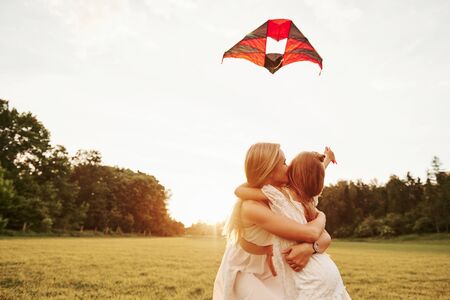 Cute family photo. Mother and daughter have fun with kite in the field. Beautiful nature.の写真素材