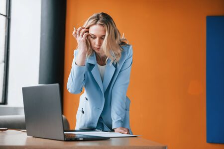 Equipment is on the table. Businesswoman with curly blonde hair indoors in room with orange colored wall.の写真素材