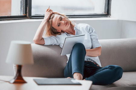 Its important to make notes. Businesswoman with curly blonde hair sitting in room against window.