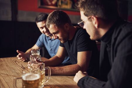 Three male friends in the bar. Supporting sad friend. Unity of people. With beer on the table.の写真素材