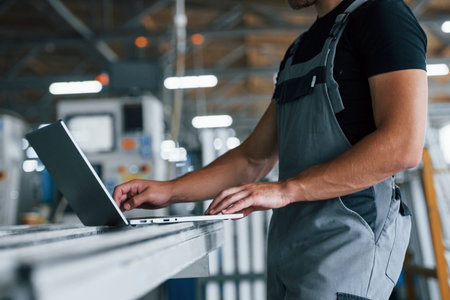Modern laptop. Typing on keyboard. Industrial worker indoors in factory. Young technician with...