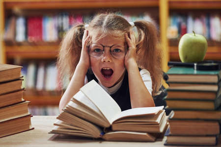 Feels excited. Cute little girl with pigtails is in the library. Apple on the books.の写真素材