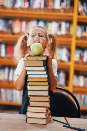 Cute little girl with pigtails is in the library. Apple on the books.の写真素材