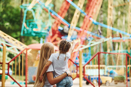 Embracing each other. Cheerful little girl her mother have a good time in the park together near attractions.の写真素材