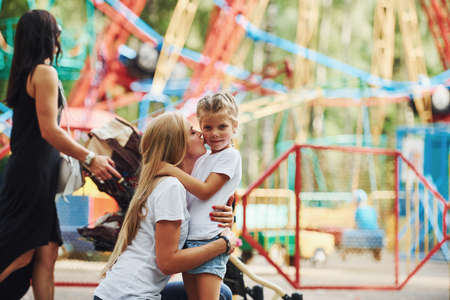 Embracing each other. Cheerful little girl her mother have a good time in the park together near attractions.の写真素材