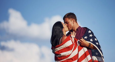Kissing each other. Feels freedom. Beautiful couple with American Flag have a good time outdoors in...