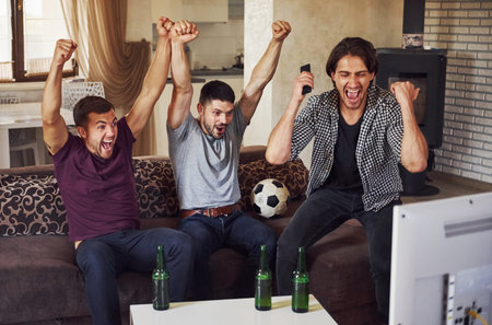 Its a goal. Excited three friends watching soccer on TV at home together.