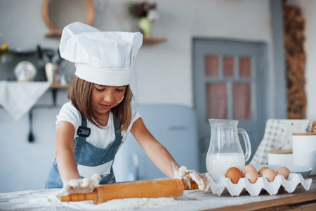 Cute kid in white chef uniform preparing food on the kitchen.