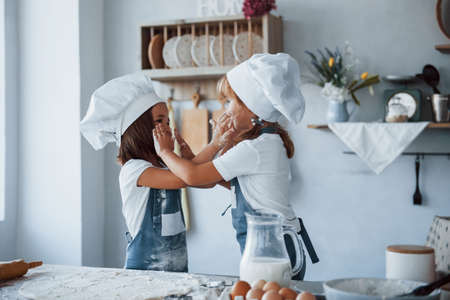 Having fun during the process. Family kids in white chef uniform preparing food on the kitchen.の写真素材