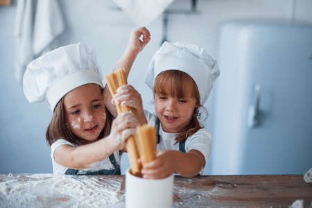 Having fun with spaghetti. Family kids in white chef uniform preparing food on the kitchen.の写真素材
