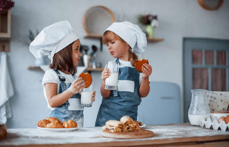 Wth glasses with milk. Family kids in white chef uniform preparing food on the kitchen.の写真素材