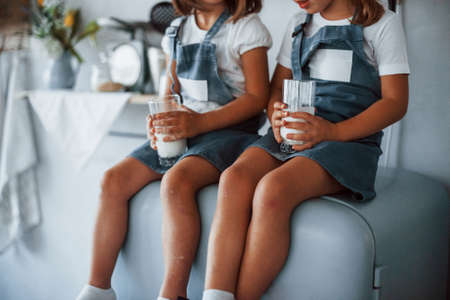 Sitting on the fridge. Family kids in white chef uniform eats food on the kitchen.の写真素材