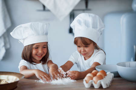 Concentrating at cooking. Family kids in white chef uniform preparing food on the kitchen.の写真素材