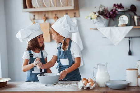 Family kids in white chef uniform preparing food on the kitchen.