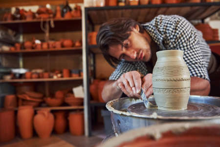 Detailing by special tool. Ceramist uses potters wheel and creates a handmade clay product.の写真素材
