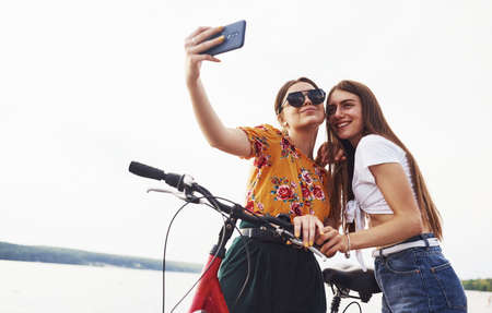 Making a selfie. Two female friends on the bike have fun at beach near the lake.の写真素材