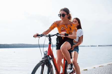 Two female friends on the bike have fun at beach near the lake.の写真素材