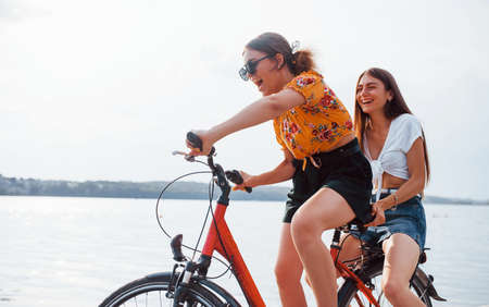 Two female friends on the bike have fun at beach near the lake.の写真素材