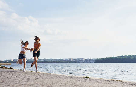 Two female friends runs and have fun at beach near the lake at sunny daytime.の写真素材