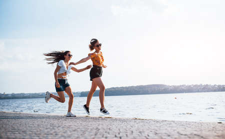 Two female friends runs and have fun at beach near the lake at sunny daytime.の写真素材