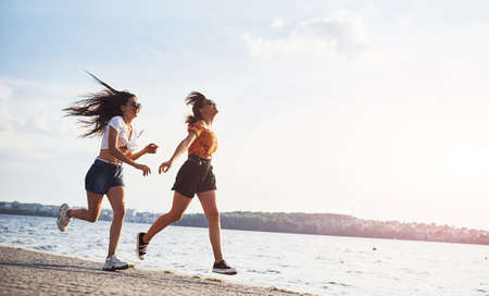 Two female friends runs and have fun at beach near the lake at sunny daytime.の写真素材