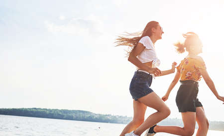 Two female friends runs and have fun at beach near the lake at sunny daytime.の写真素材