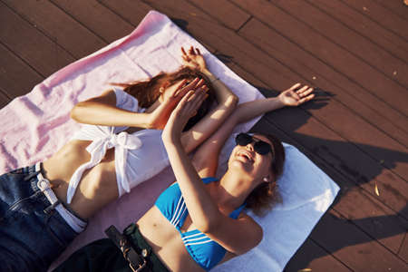Gives high five. Top view of two girls on the beach that lying down on the ground and enjoying warm sunlight.の写真素材