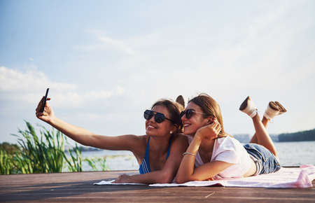 Two girls on the beach lying down on the ground and enjoying warm sunlight.の写真素材