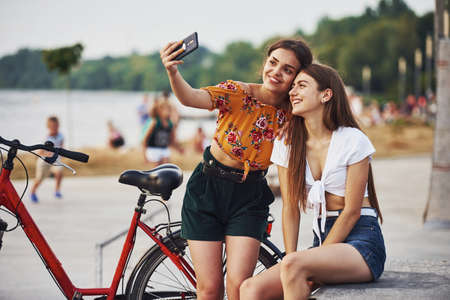 Making a selfie. Two young women with bike have a good time in the park.の写真素材