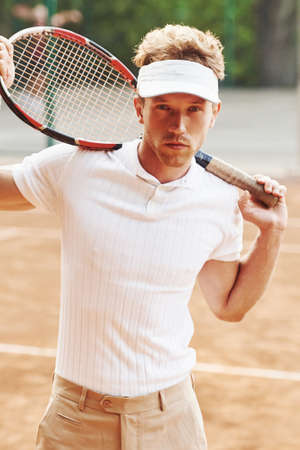 Posing for a camera. Young tennis player in sportive clothes is on the court outdoors.の写真素材