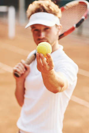 Holds ball in hand. Young tennis player in sportive clothes is on the court outdoors.の写真素材